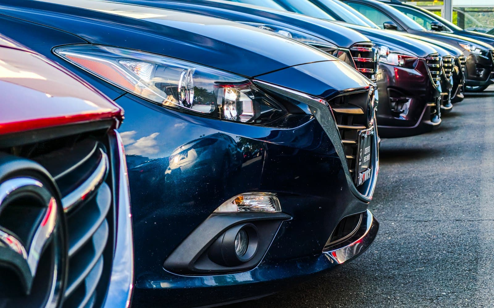 Stock photo of a row of cars lined up at a dealership, front grilles and headlights in close-up