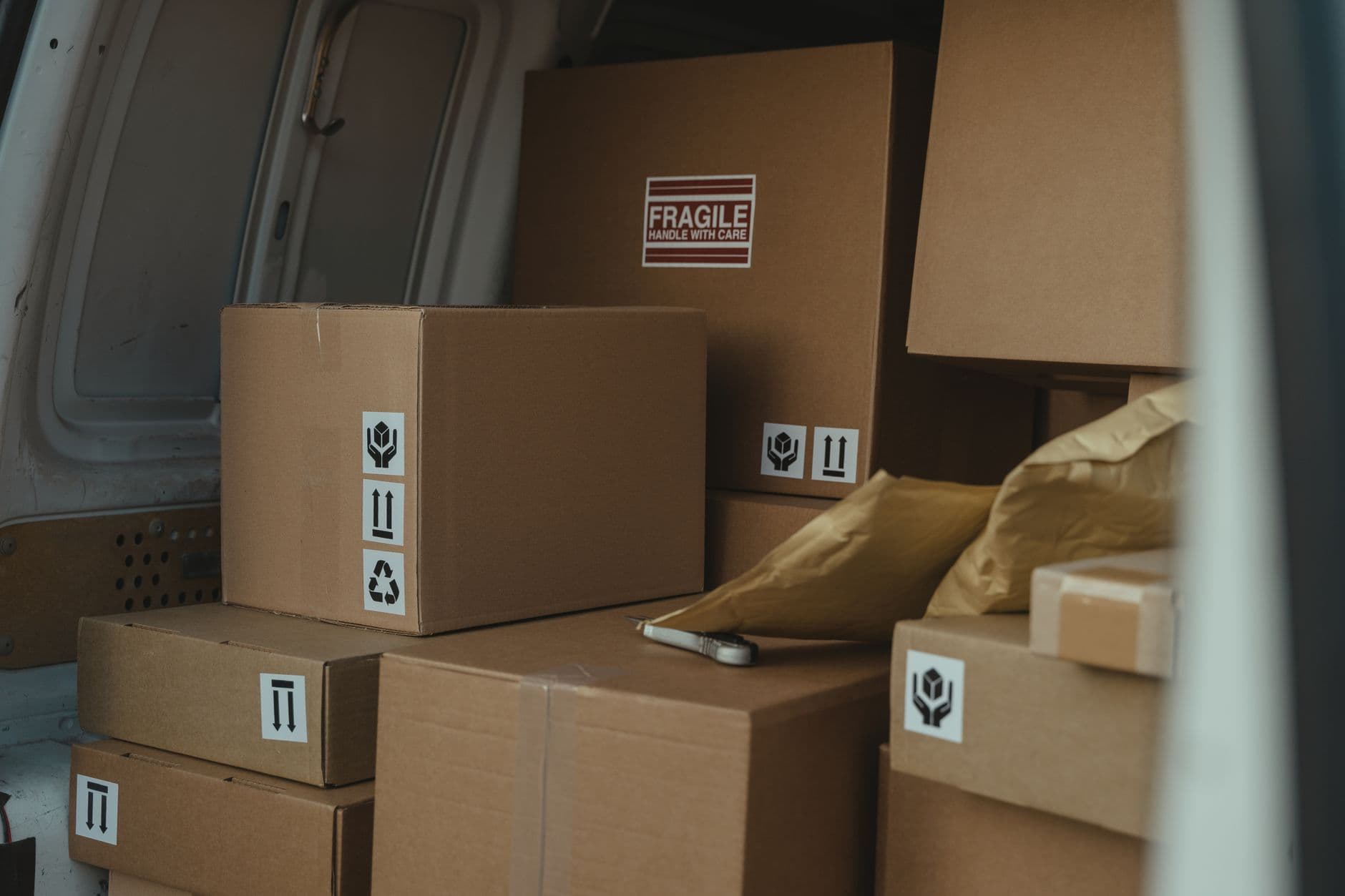 Stock photo of cardboard parcels, one labeled fragile, stacked in the back of a delivery van